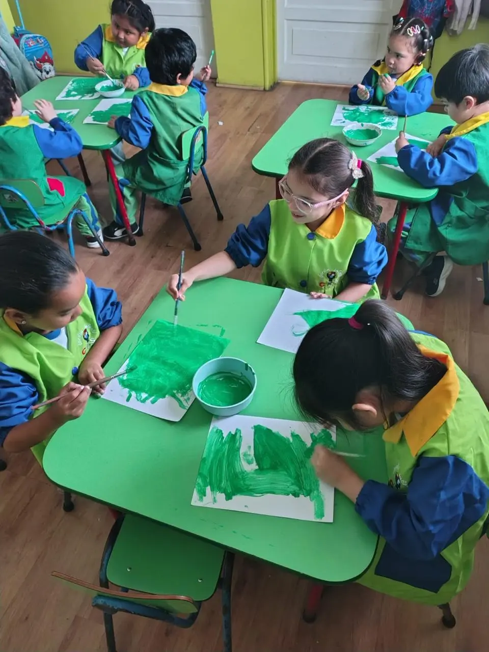 Niños de Transición Menor experimentan con pintura verde en sus mesas de trabajo